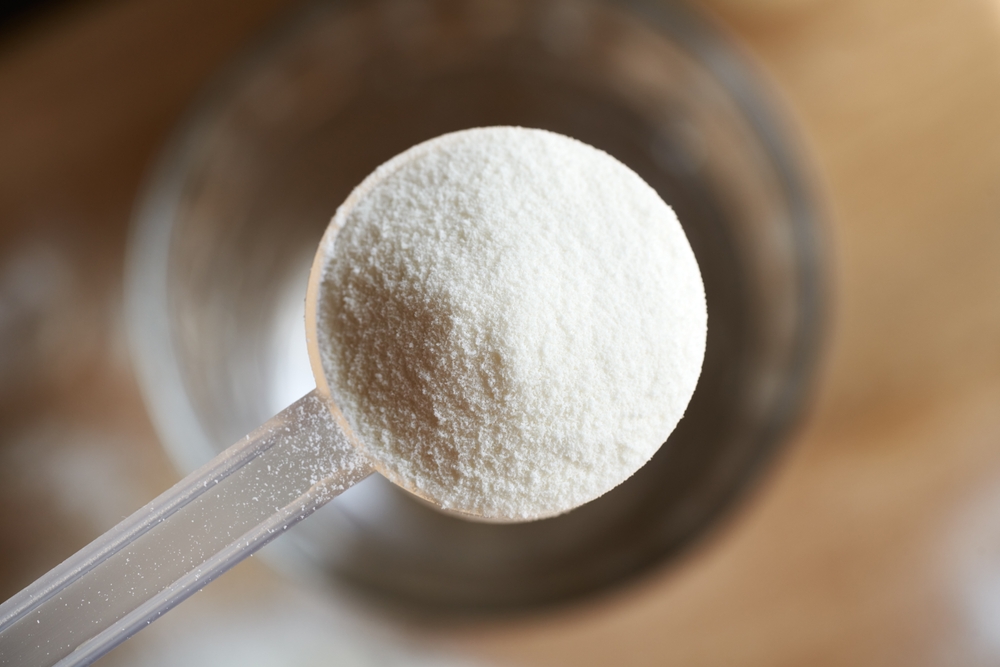 Collagen,Powder,In,A,Plastic,Measuring,Spoon,Above,A,Glass